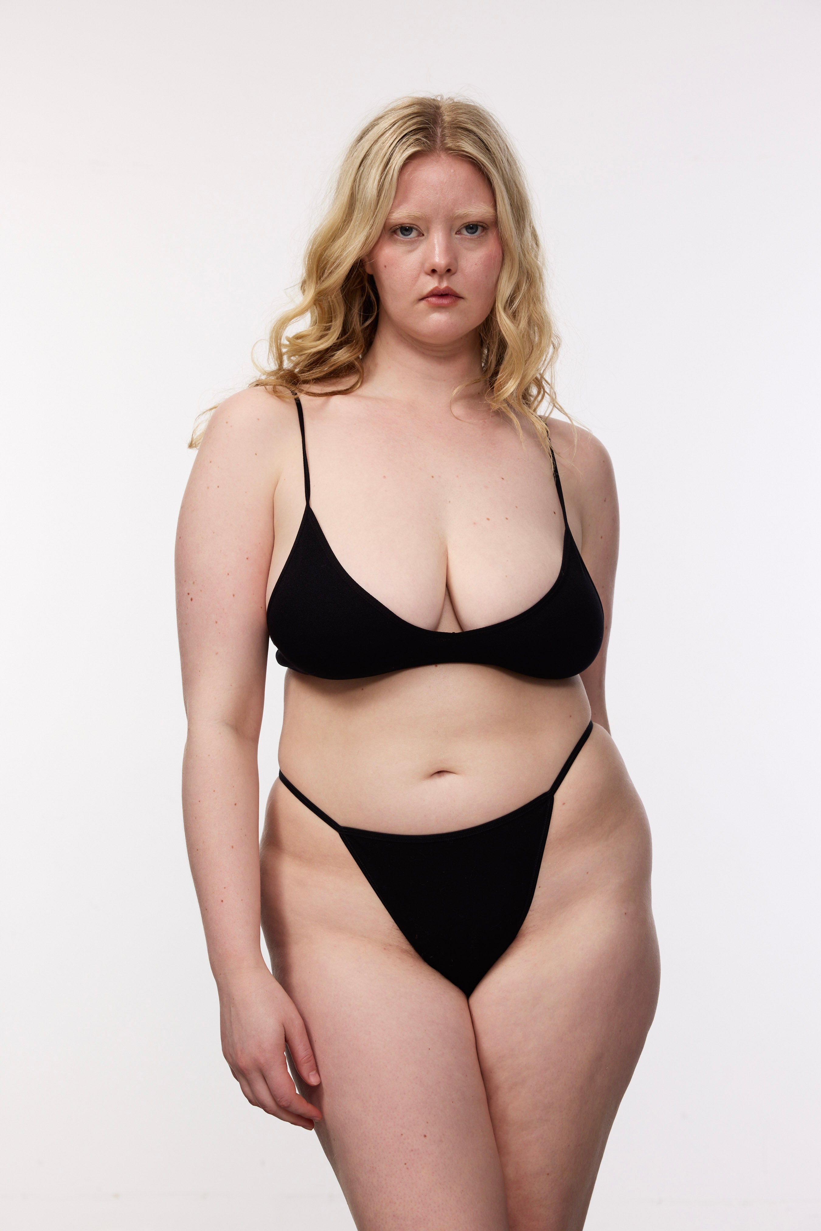 Plus size model wearing black g-string and bralette, front view
