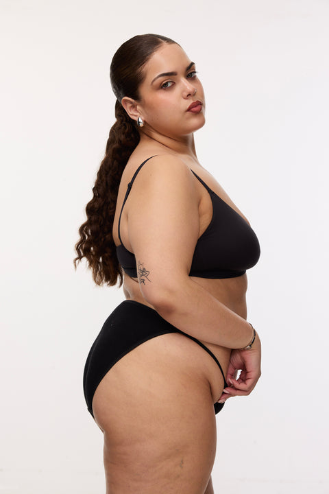 Plus size model wearing black bikini brief and bralette, side view