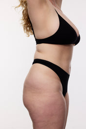 Plus size model wearing black mid-rise thong and bralette, three-quarter view