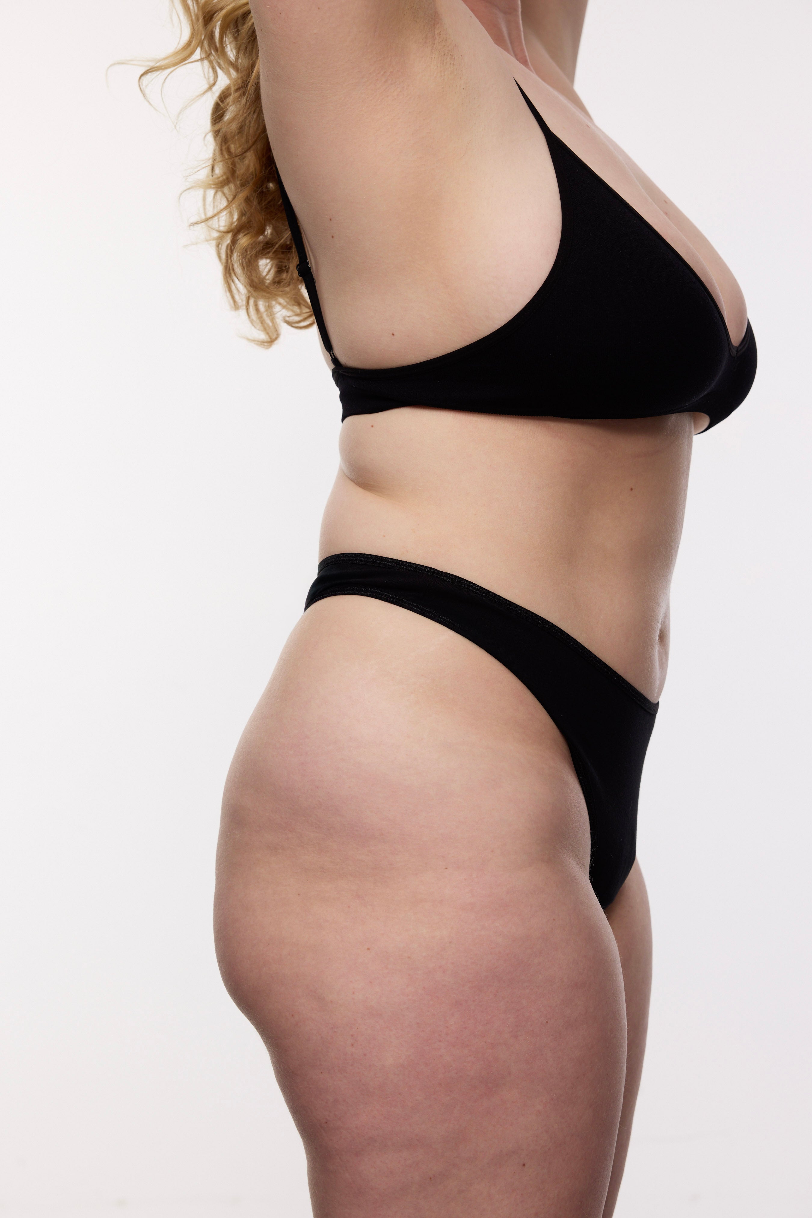 Plus size model wearing black mid-rise thong and bralette, three-quarter view