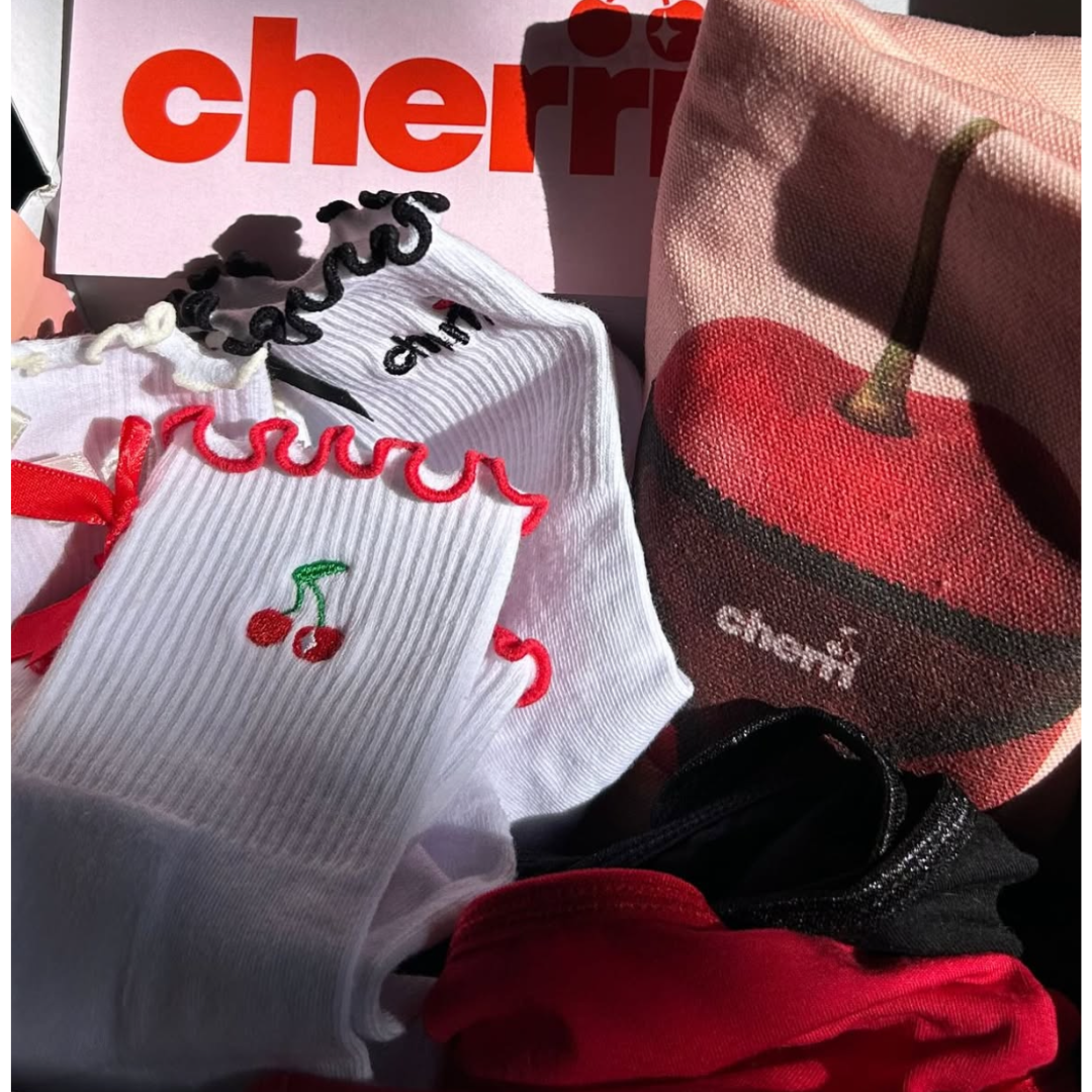 Cherri Ruffle Pilates Grip Socks lifestyle flat lay - white socks with cherry embroidery and cherri logo alongside pink Cherri Tote and cherry-themed packaging