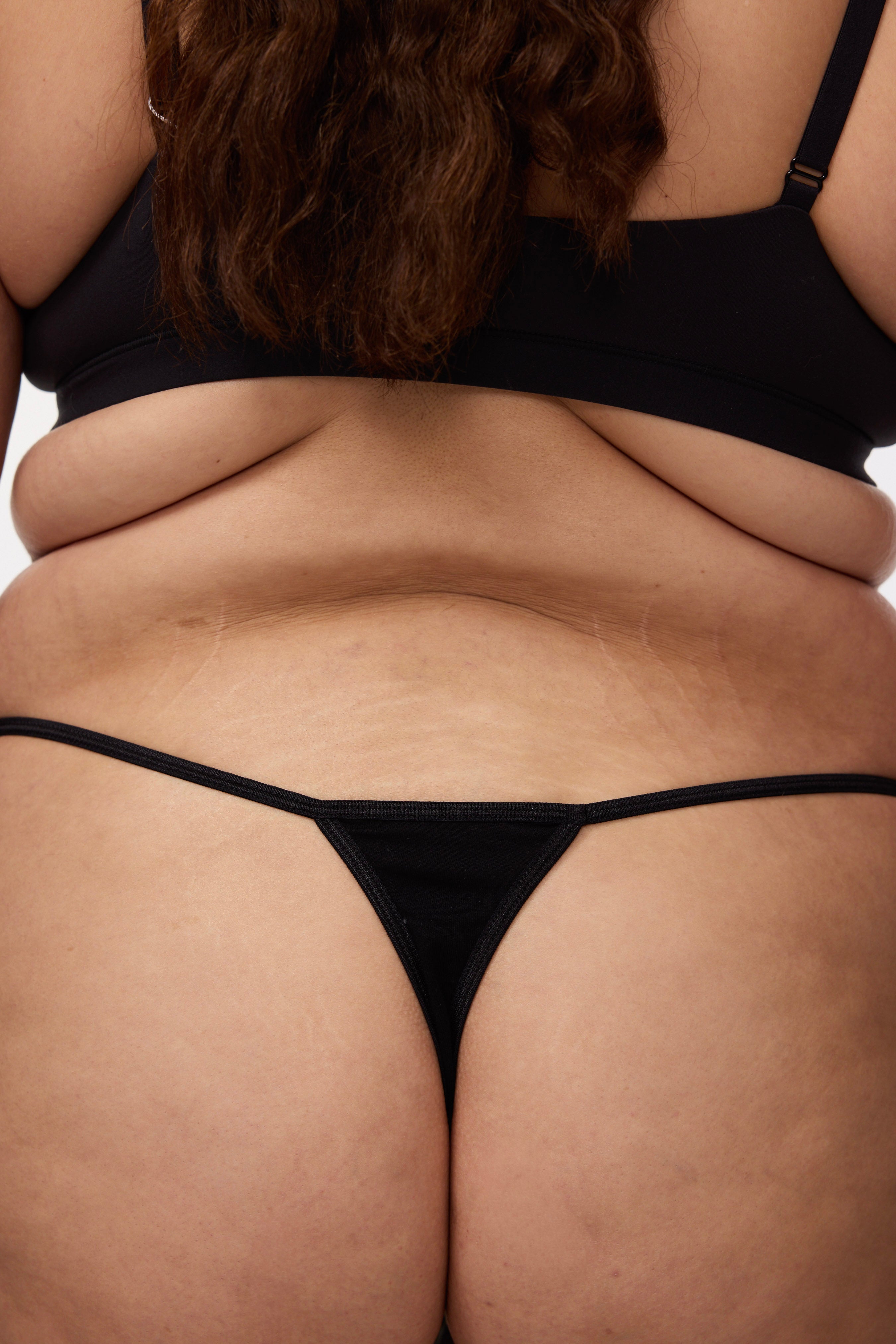 Plus size model wearing black g-string and bralette, back view