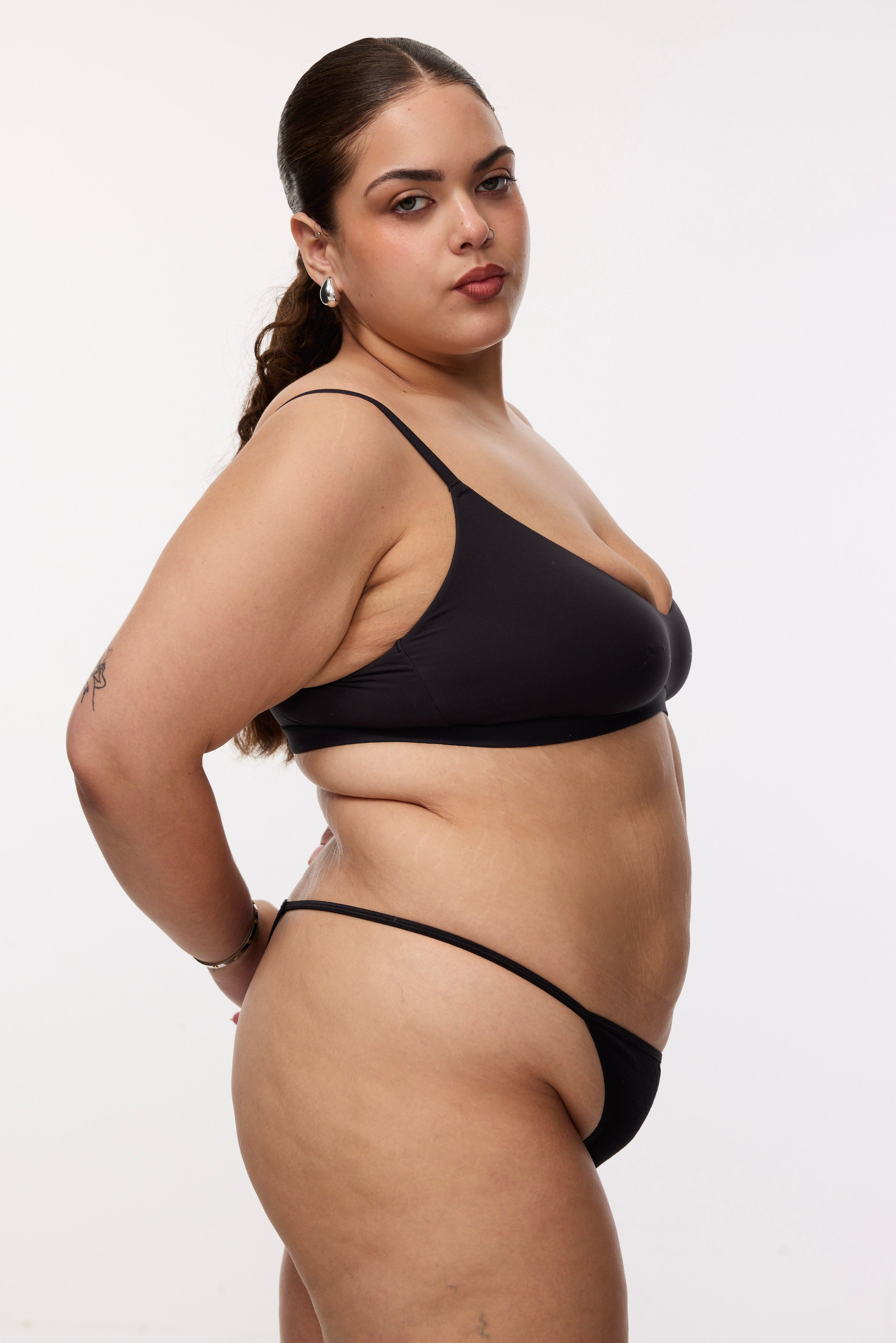 Plus size model wearing black g-string and bralette, side view